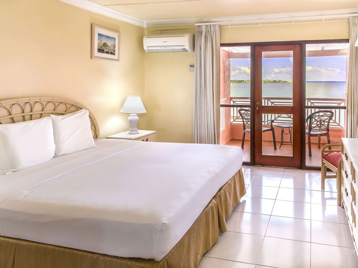 A hotel room with a large bed, two nightstands, a dresser, a balcony door opening to a terrace, and a seating area by the window.